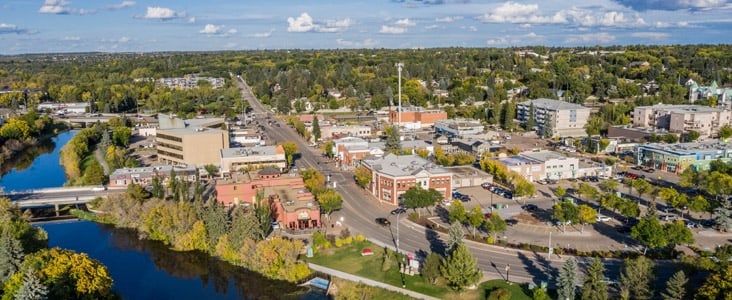 Aerial view of a small city with a river, bridges, streets, and buildings under a partly cloudy sky.