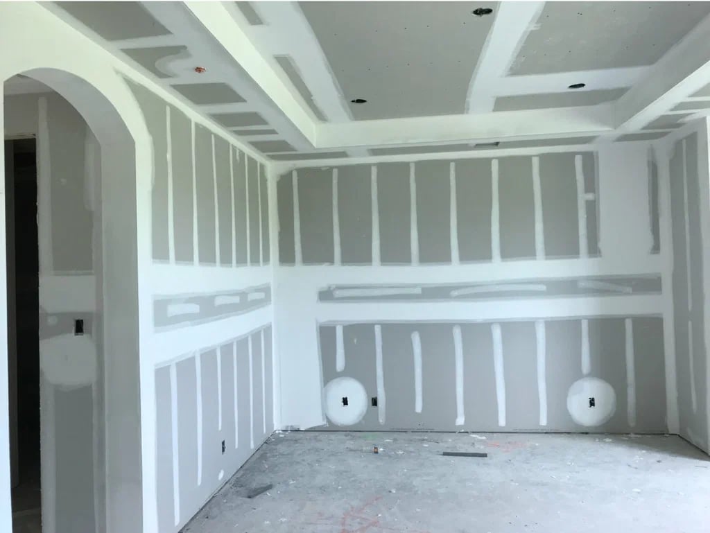 Unfinished room with white drywall panels and patches on walls and ceiling, and bare concrete floor.