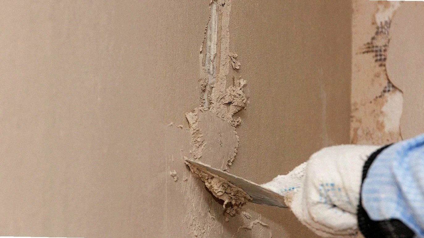 Hand in glove applying plaster to a wall with a trowel during wall repair.