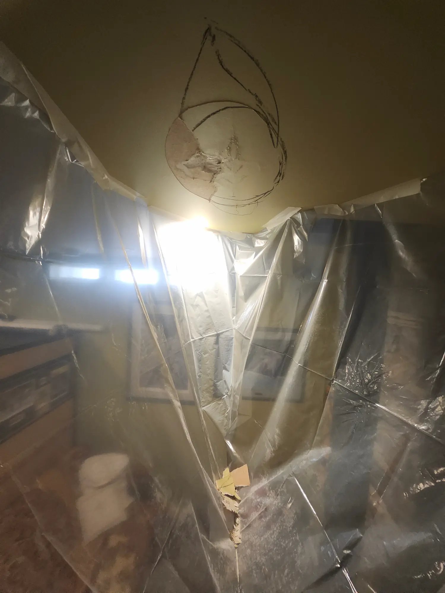 Room under repair with plastic sheets hanging and ceiling damage with a marked outline.