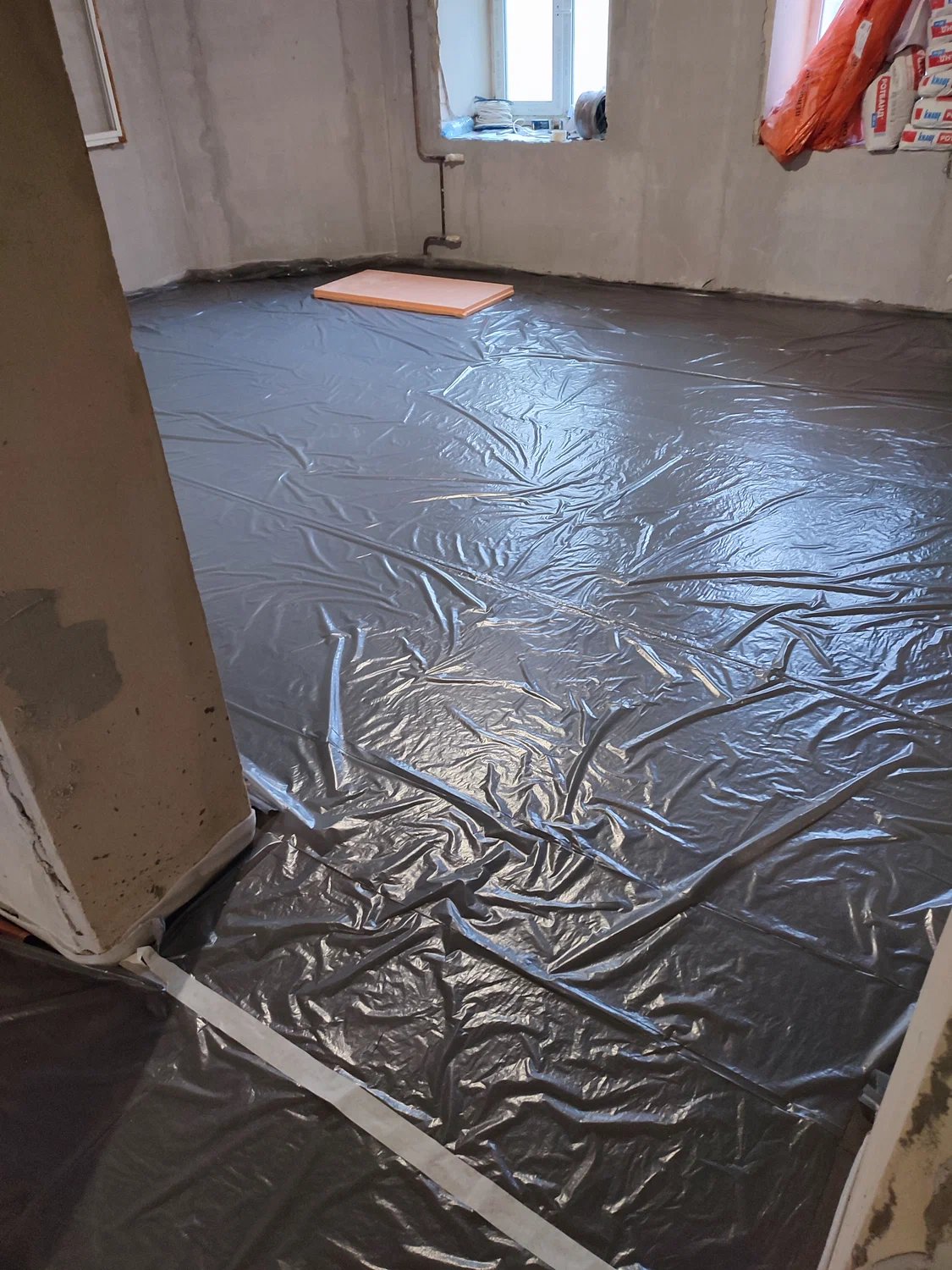 Room under construction with plastic sheeting taped on the floor and unfinished walls.