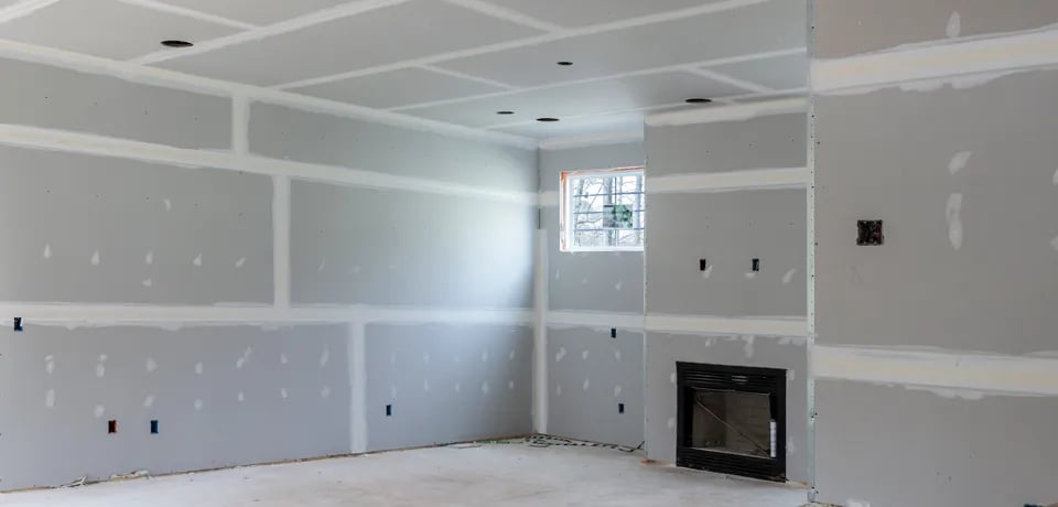 Interior room under construction with drywall installed and taped, small window, and fireplace insert.